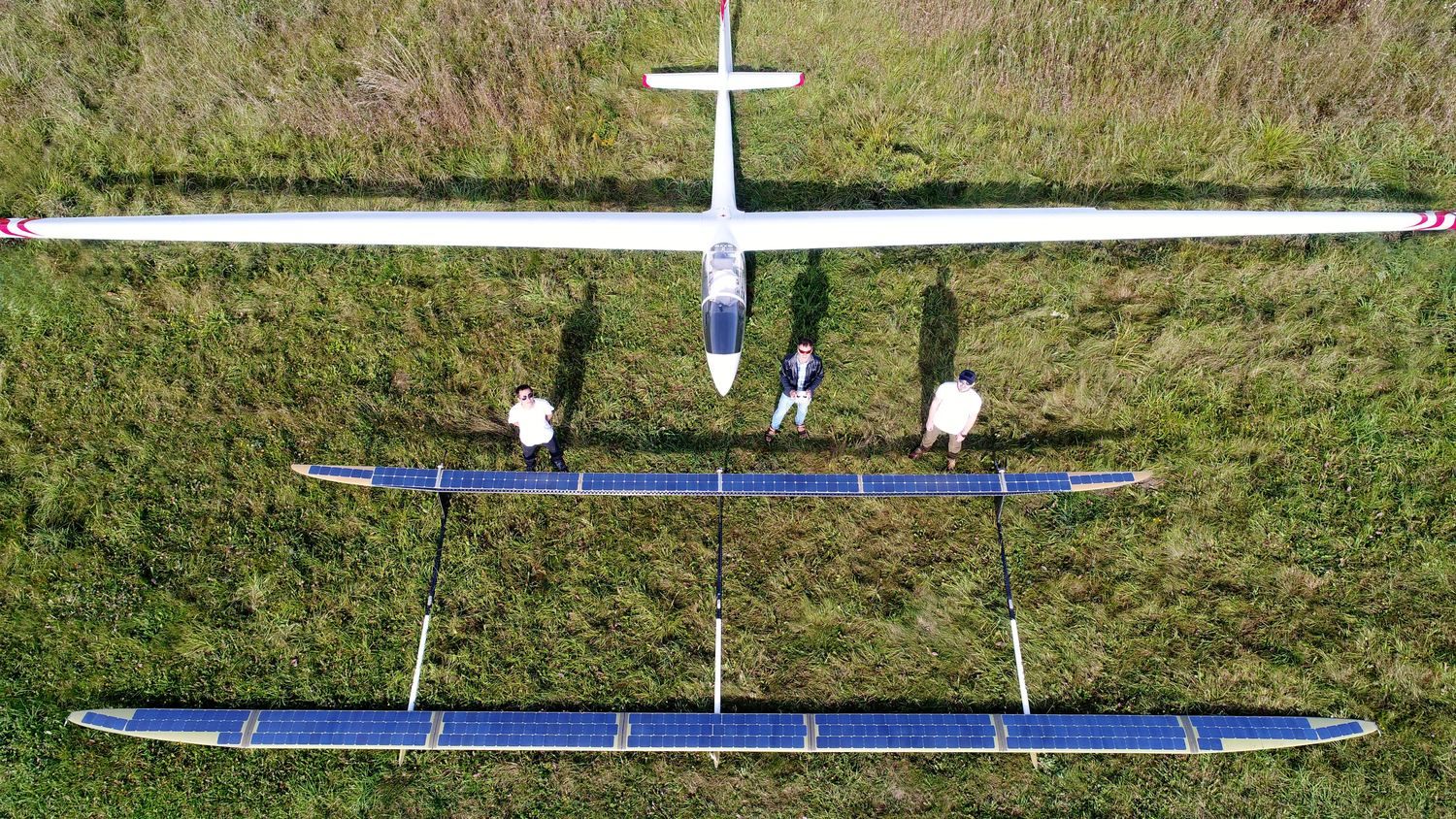 Aerial view of the ApusDuo tandem-wing solar aircraft on a grass field with its ground crew