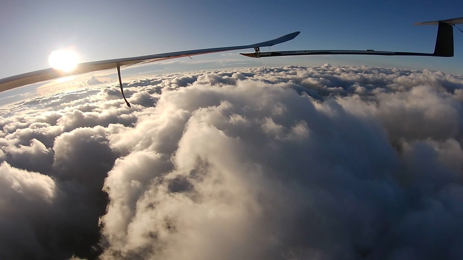 The HAPS wing above towering clouds with the sun low on the horizon